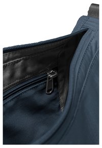 Gros plan de l'intérieur d'un sac en tissu bleu marine montrant une poche zippée noire avec un curseur de fermeture éclair en métal.