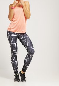 Letvægts koral tanktop parret med sorte leggings med et geometrisk hvidt mønster. Sorte træningssko med neonlys fuldender looket.