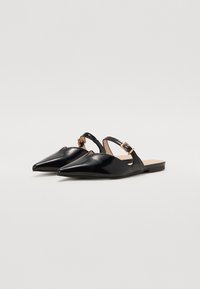 Ballerines noires en cuir verni, avec un bout pointu, des découpes sur les côtés et une fermeture par boucle dorée sur la bride de la cheville. Semelle plate.