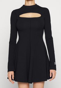 Svart långärmad klänning med hög halsringning och en utskärning vid bröstet. Omlott kjoldesign, tillverkad av ett mjukt, stretchigt material.