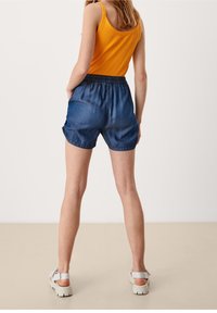 Shorts di jeans con cintura elastica, caratterizzati da una vestibilità ampia e orlo arrotolato. Abbinati a una canotta a coste di un vivace giallo.