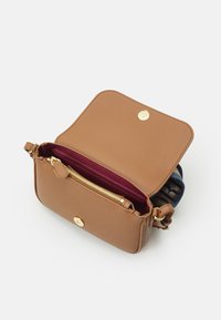 Skórzana torba na ramię w kolorze brązowo-tanowym z teksturowaną powierzchnią, wewnętrzną kieszenią na zamek i złotymi detalami. Otwarta klapka odsłania ciemnoczerwoną podszewkę.