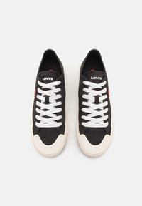 Černé plátěné tenisky s bílými šněrovadly a krémovou gumovou podrážkou. Na jazyku je logo "LEVI'S". Zaoblený design špičky.