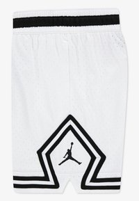 White athletic shorts with black accents, featuring a perforated texture, an elastic waistband, and a prominent black Jumpman logo on a star design.