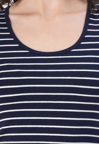 Námořnická modrá a bílá pruhovaná bavlněná tílko s kulatým výstřihem. Pruhy jsou rovnoměrně rozložené a látka vypadá měkká a hladká.
