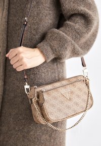 Beige crossbody-taske med mønster, guldfarvet hardware, lynlåslukning og kæderem. Tekstureret materiale med logo-accenter foran.