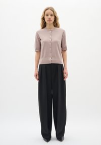 Helles rosa kurzärmeliges Cardigan mit Knöpfen, kombiniert mit lockeren schwarzen Hosen, die eine hohe Taille und ein gepunktetes Design aufweisen.