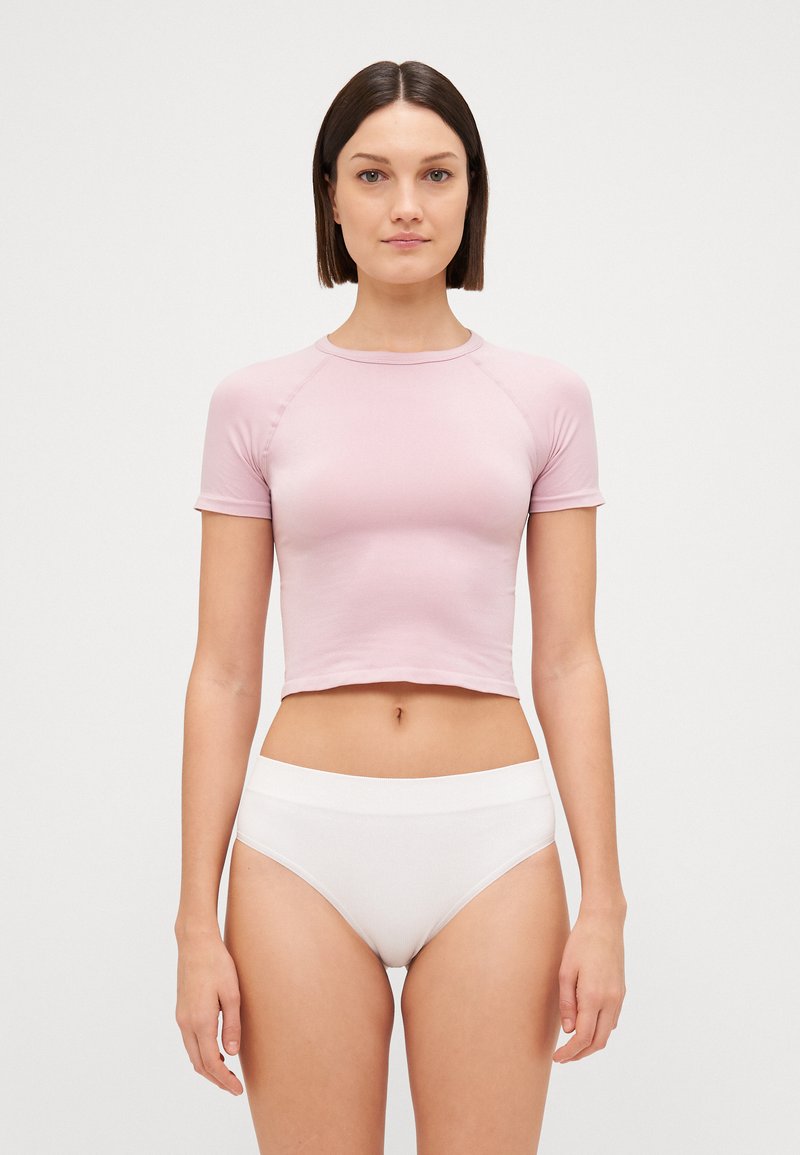 Un haut rose clair court avec des manches courtes, fabriqué en tissu lisse ; associé à des culottes blanches taille haute, les deux sans embellissements et ajustées.