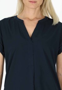 Himmelblaues kurzärmliges Blusenshirt mit V-Ausschnitt, aus weichem Stoff und einer Knopfleiste vorne. Subtile Textur, lockere Passform.