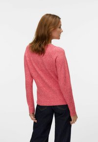 Pull en maille texturée rose à manches longues et ourlet côtelé, doté d'un col ras du cou classique. Porté avec un pantalon en denim foncé.