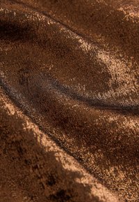 Brown velvet fabric featuring a textured surface with a slight sheen, displaying variations in color and depth throughout the material.