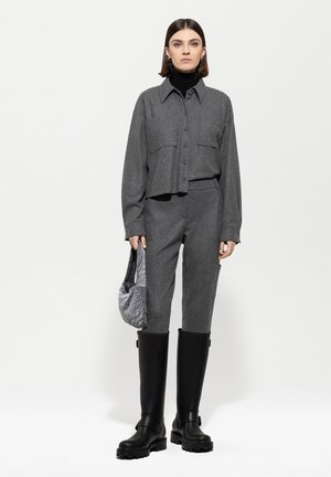 Grau strukturierte, kurze Bluse mit Knopfdetails, passende graue Hose, schwarze hohe Stiefel und eine graue Handtasche. Sauberes, modernes Design.