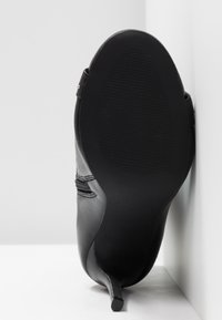 Scarpa nera con tacco alto, in pelle liscia, punta affusolata e tacco sottile. La suola presenta una superficie testurizzata e antiscivolo.