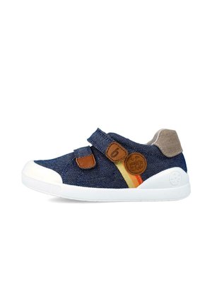 Zapato de denim azul con suela de goma blanca, acentos de cuero marrón, dos correas de velcro y un detalle de rayas multicolores en el costado.