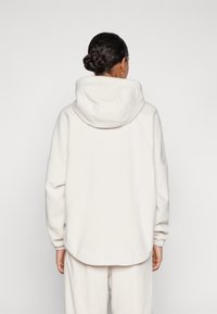 Felpa bianca con cappuccio, dalla vestibilità ampia, tessuto testurizzato e spalle scese. Design minimalista senza loghi o motivi visibili.