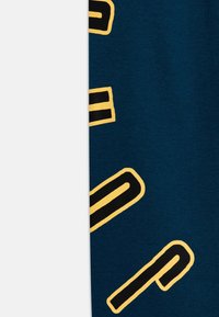 Marineblauer Stoff mit schwarzen und gelben geometrischen Mustern. Die Textur wirkt glatt und leicht elastisch. Sichtbare gedruckte Akzente.