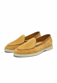 Zamszowe loafers w musztardowym żółtym kolorze z gładką brązową skórzaną lamówką. Posiadają okrągły nos i białą gumową podeszwę. Płaski design.