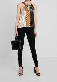 Top halter multicolore con dettagli a chiave, caratterizzato da tonalità di marrone, bianco, nero e pois; abbinato a jeans skinny neri e tacchi.