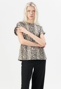 Short-sleeve, loose-fitting top with a beige and black snake print pattern, featuring a textured fabric and a rounded hem. Paired with black trousers.