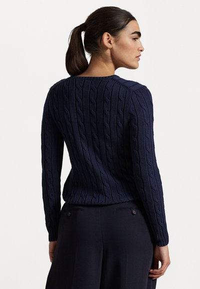 Suéter de punto de cable azul marino con mangas largas, que presenta un patrón texturizado y un cuello redondo, combinado con pantalones oscuros ajustados.