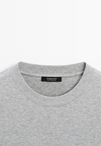 Pull gris clair à col rond avec col côtelé et une étiquette noire à l'intérieur du col indiquant "Massimo Dutti, Fabriqué au Portugal."