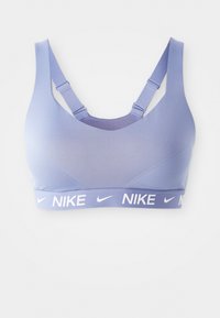 Sostén deportivo Nike de color púrpura claro con tirantes ajustables y banda elástica con logo en el borde inferior, sobre fondo blanco.