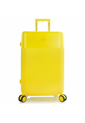 Maleta rígida de color amarillo brillante con mitad inferior acanalada, asa telescópica y cuatro ruedas giratorias dobles sobre fondo blanco.