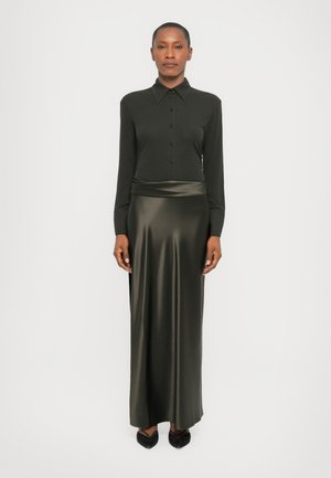 Langsleeve, knoop-ups hem in donkergroene stof, gecombineerd met een slanke, hoge taille, satijnen olijfgroene rok. Zwarte puntige ballerina's maken de look af.