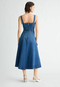 Denim-Midikleid mit tailliertem Oberteil, breiten Trägern, Reißverschluss, tailliertem Bund und ausgestelltem Rock. Auffällige blaue Farbe und sichtbare Nähte.