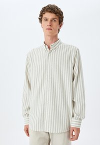 Camisa de manga larga abotonada en crema claro con sutiles rayas grises. Presenta un cuello clásico y mangas con puños, con acentos de rayas horizontales.