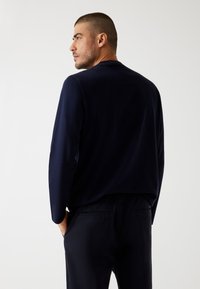 Top a maniche lunghe blu navy con scollo rotondo, caratterizzato da una superficie liscia. Indossato con pantaloni coordinati, presenta una vestibilità comoda.
