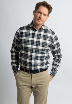 Button-down geruite blouse in marineblauw, wit en groen met lange mouwen, gedragen met kaki broek en een zwarte riem. Strakke, gestructureerde uitstraling.