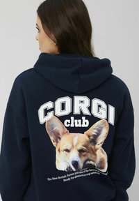 Hoodie marin avec le texte "CORG I club" et un graphique d'un corgi endormi, avec une texture douce et une capuche ajustable.