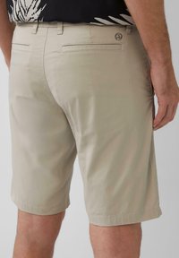 Shorts en coton beige avec une texture lisse, coupe droite et poches arrière. Petit logo sur la ceinture.