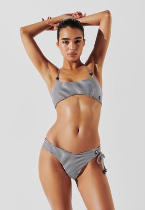 Bikini a due pezzi a strisce in bianco e nero. Il top presenta spalline regolabili, mentre il fondo ha un dettaglio annodato di lato. Tessuto liscio.