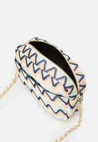 Crossbodytas met rits in een chevronpatroon in pastelkleuren, gemaakt van gestructureerde stof, met een gouden kettingriem en een zwarte binnenkant.