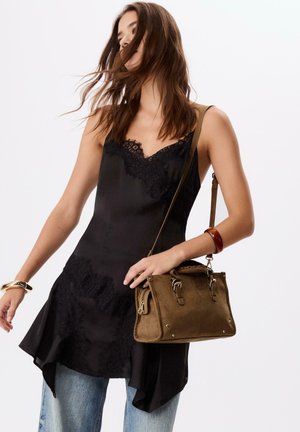 Camisole en satin noir avec bordure en dentelle et ourlet asymétrique, associé à un sac à main en suède marron avec des accents métalliques et une bandoulière.