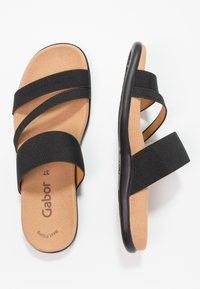 Paire de sandales à semelle beige avec trois brides élastiques noires, une large et deux étroites, vues de dessus et de côté.
