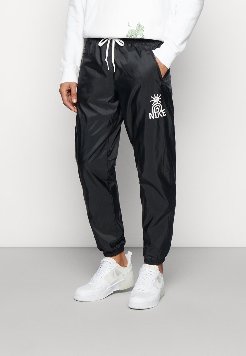 Svarta nylonjoggers med elastiska mudd, med en vit grafisk logotyp och dragsko i midjan. Matchas med vita sneakers för en sportig look.