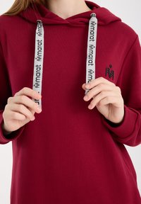 Bordeauxrode hoodie met een voorzak, voorzien van grijze trekkoorden met zwarte tekst. Gladde stof met een ontspannen pasvorm en geribbelde manchetten.
