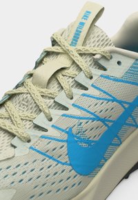 Lys grå Nike-løpesko med blå swoosh, pustende mesh-overdel og kremfargede lisser knyttet over tungen.