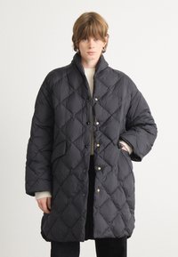 Zwarte gewatteerde pufferjas met diamantpatroon, knoopsluitingen, hoge kraag en zijzakken. Glad textuur en oversized pasvorm.