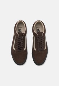 Brązowe zamszowe trampki z kremowymi bocznymi paskami i czarnymi gumowymi podeszwami. Charakteryzują się zaokrąglonym noskiem, dopasowanymi sznurowadłami oraz klasycznym wzornictwem.