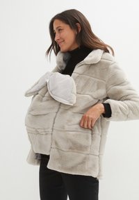 Giacca premaman in pelliccia sintetica di colore grigio chiaro, con chiusura a zip, colletto oversize e tasca frontale con un morbido coperchio imbottito.