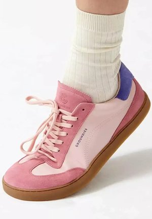 Pied en chaussette blanche portant une sneaker Groundies rose et violette avec semelle en gomme, vu de côté sur fond blanc.