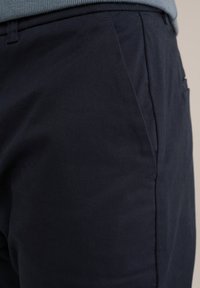 Jūras spēku bikses, izgatavotas no gludas auduma, ar pielāgotu piegriezumu, taisnām kājām un diskrētām sānu kabatām. Tīras šuves ar klasisku dizainu.