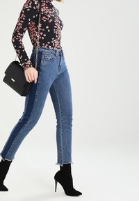 Černý top s dlouhým rukávem s květinovým vzorem, doplněný světle modrými vysokým pasem a crop džínami s nedokončeným lemem a bočními panely; černá kabelka a střevíce na podpatku.