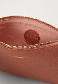 Pochette en cuir texturé rose avec une fermeture éclair dorée, dotée d'une doublure lisse et d'un logo circulaire en relief à l'intérieur.