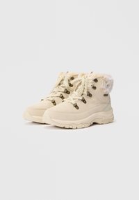 Botas de caminhada bege feitas de camurça e material sintético, apresentando colarinho de pelúcia sintética, ilhós metálicos e solas de borracha texturizada.