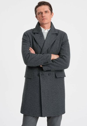Manteau en laine gris avec grands revers, devant croisé et poches plaquées. Texture douce et coupe cintrée. Porté par-dessus un pull léger.